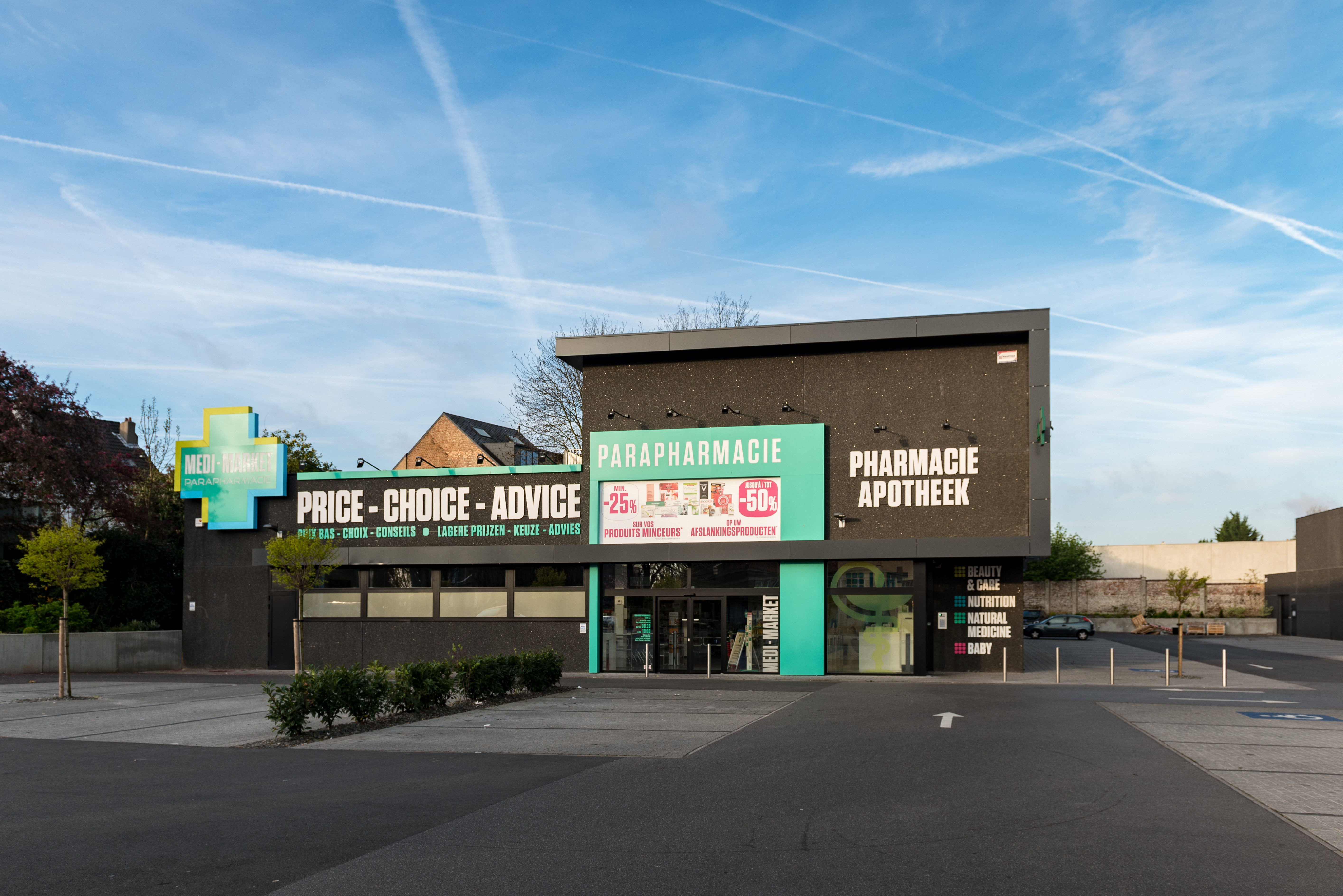 Façade d'une parapharmacie avec enseignes "Price - Choice - Advice" et "Pharmacie Apotheek", sous un ciel bleu avec traînées de nuages.