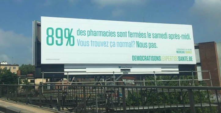 Panneau d'affichage blanc avec texte vert et bleu sur la fermeture des pharmacies le samedi après-midi, situé en extérieur avec ciel bleu en arrière-plan.