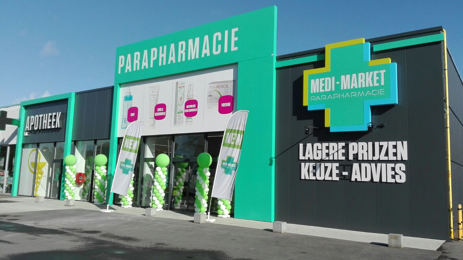 Façade d'une parapharmacie verte et noire avec des ballons verts, des affiches promotionnelles et des panneaux "Apotheek" et "Medi-Market".