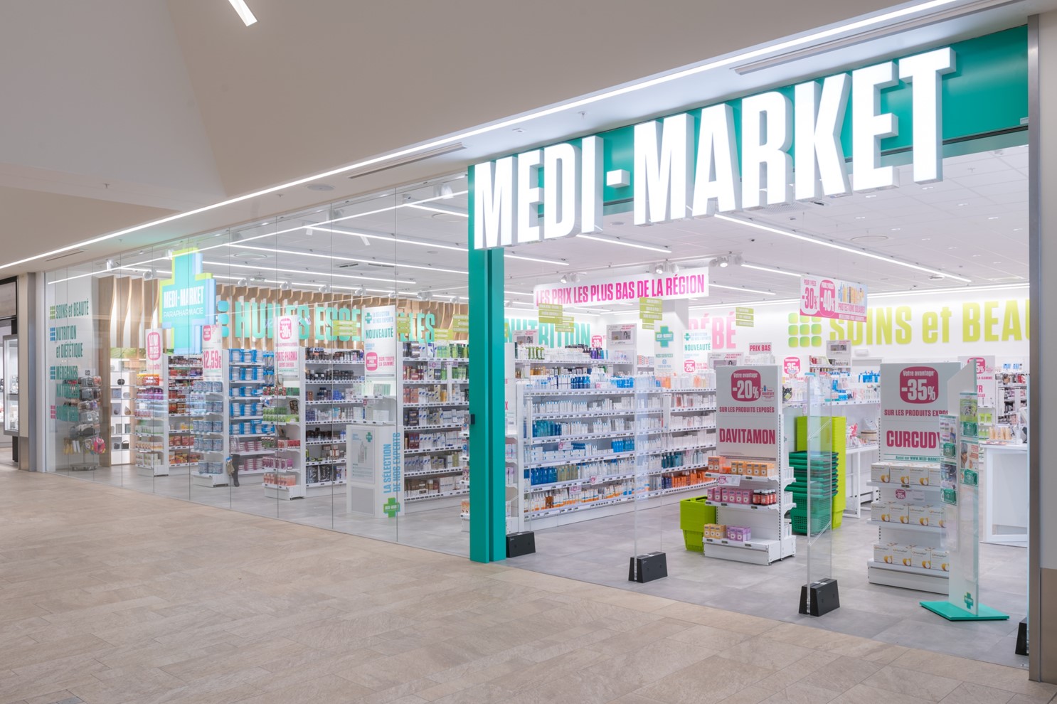 Façade d'une pharmacie Medi-Market avec des étagères de produits de santé et de beauté, affiches promotionnelles et enseigne lumineuse.