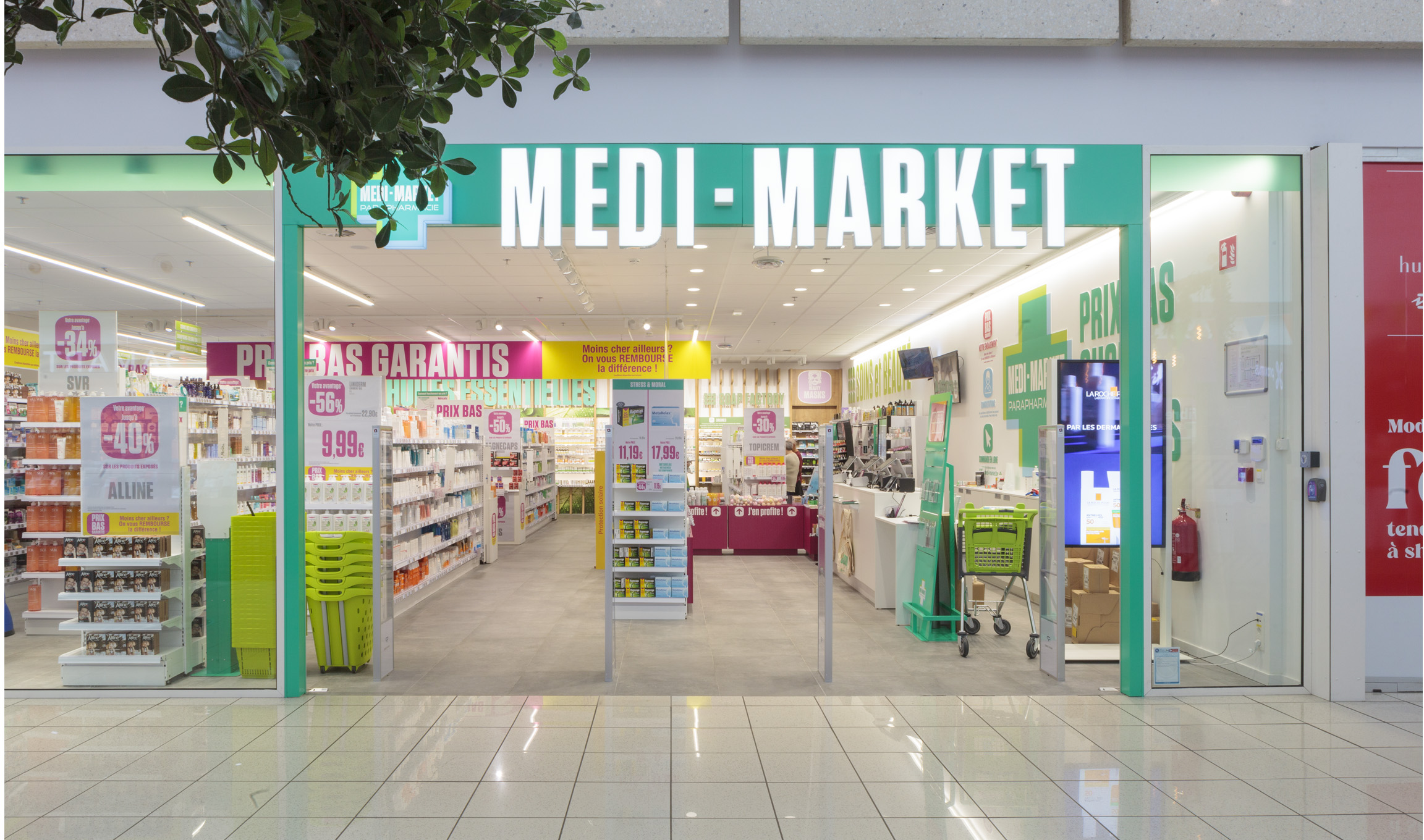 Entrée d'un magasin Medi-Market avec des panneaux promotionnels, étagères de produits de santé, et un caddie vert à l'intérieur.