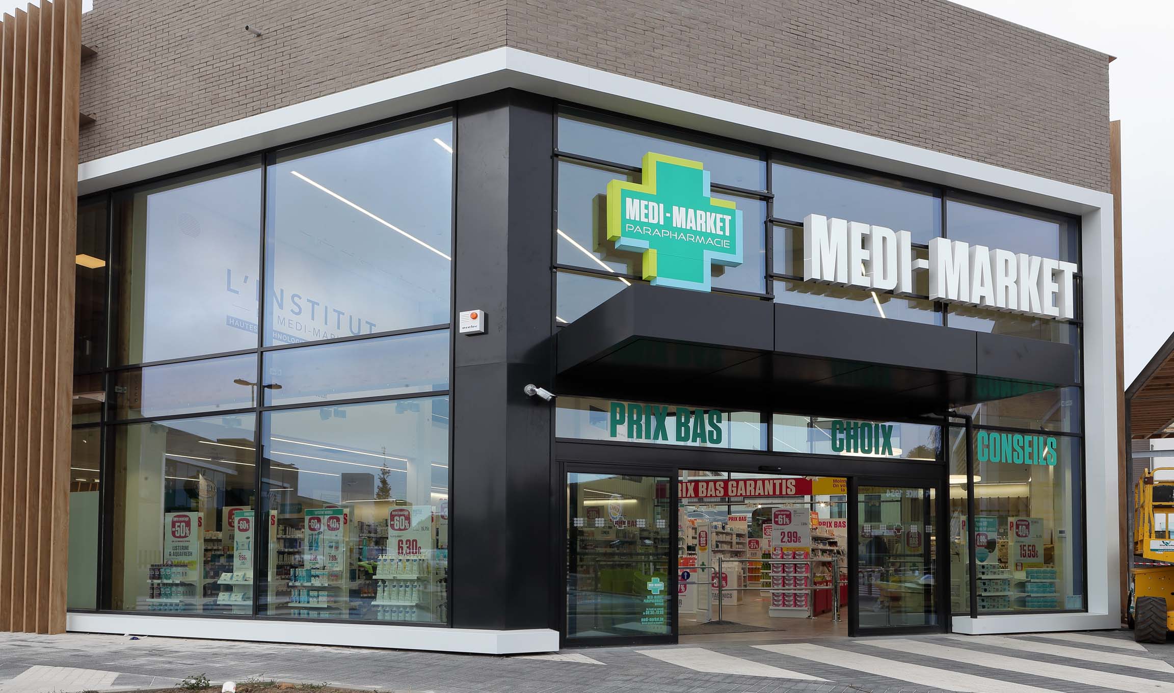 Façade d'un magasin Medi-Market avec enseigne verte et blanche, grandes vitrines, et affiches promotionnelles à l'intérieur.