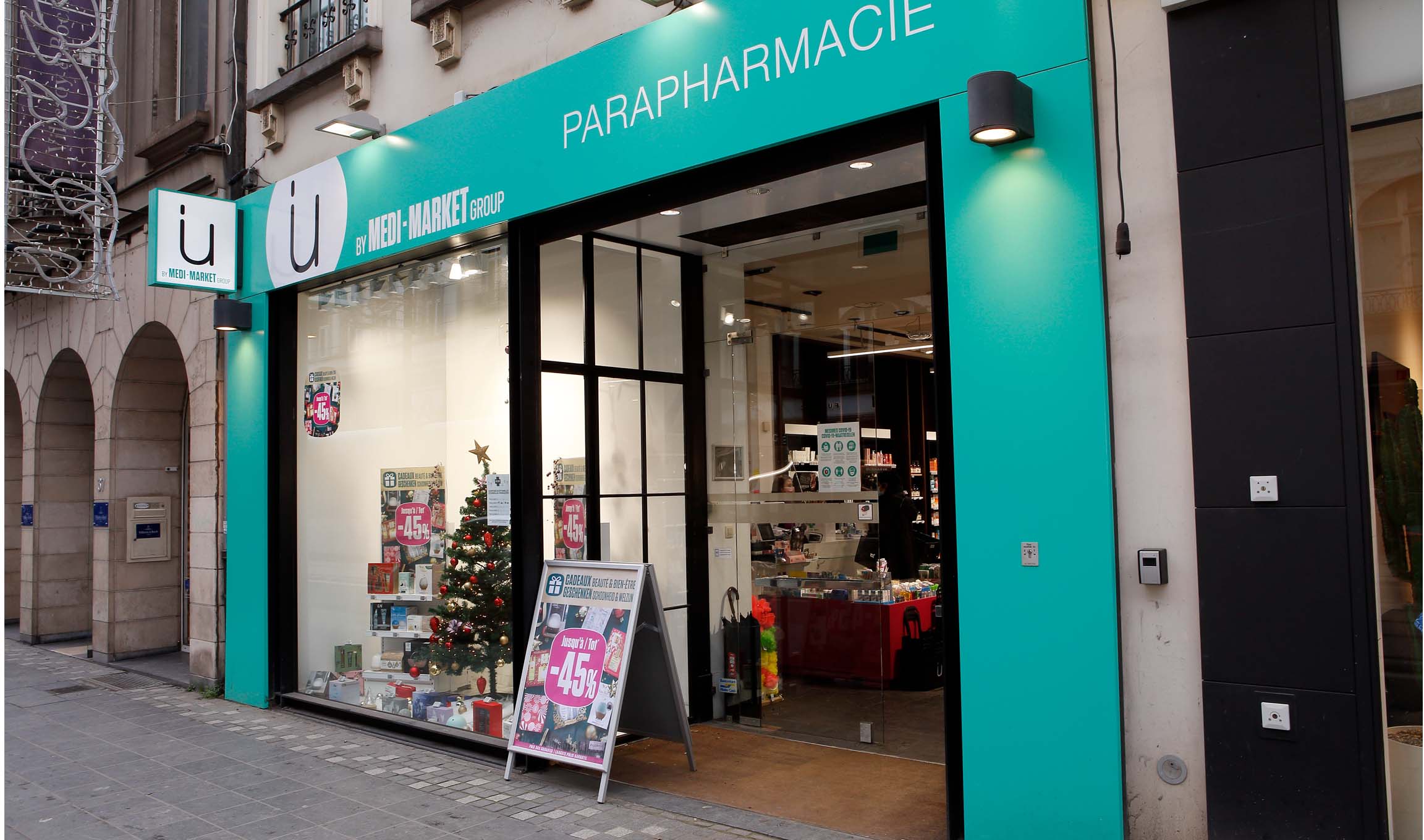 Façade d'une parapharmacie Medi-Market avec enseigne turquoise, vitrine décorée d'un sapin de Noël et panneau promotionnel à -45%.