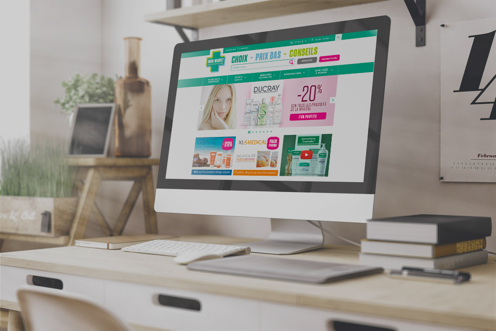 Un écran d'ordinateur affiche une page web avec des promotions de produits de santé et beauté, sur un bureau avec des plantes et des livres.