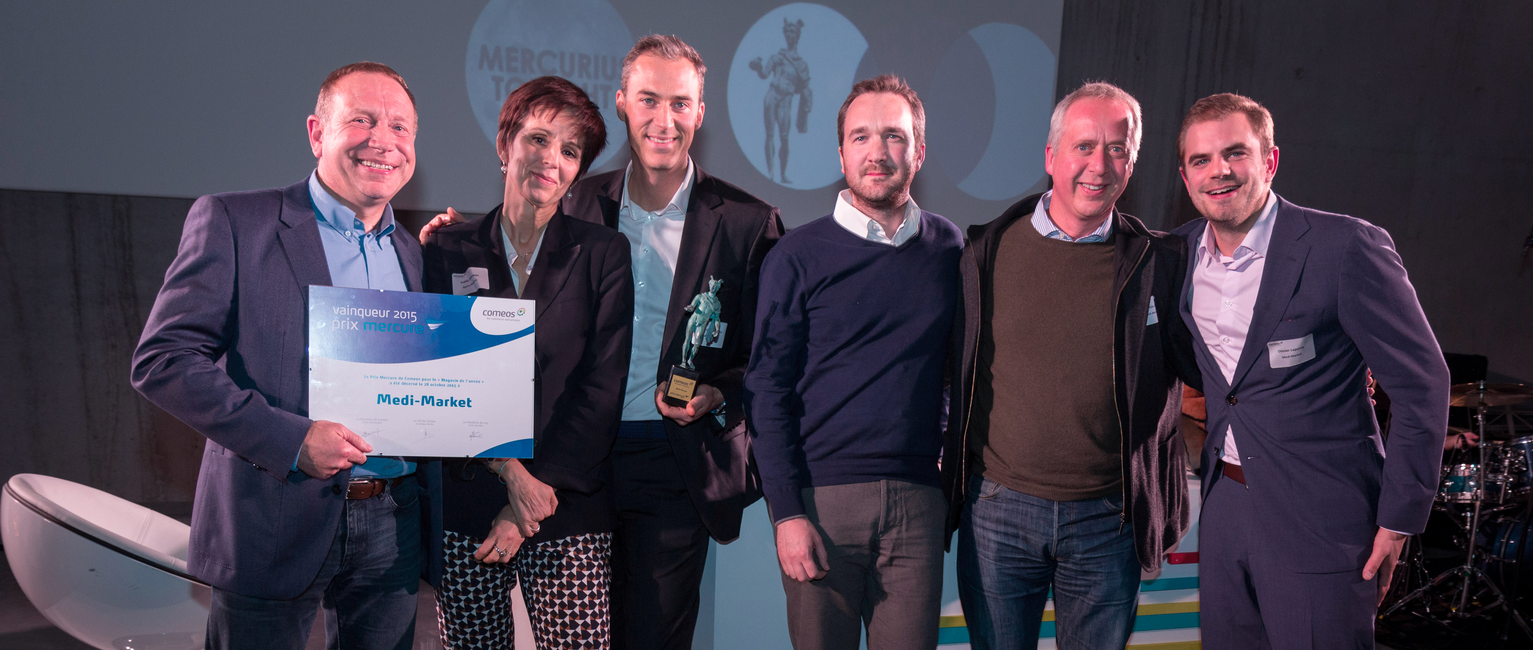 Six personnes posent avec un trophée et un certificat lors d'un événement, devant un arrière-plan avec un logo.