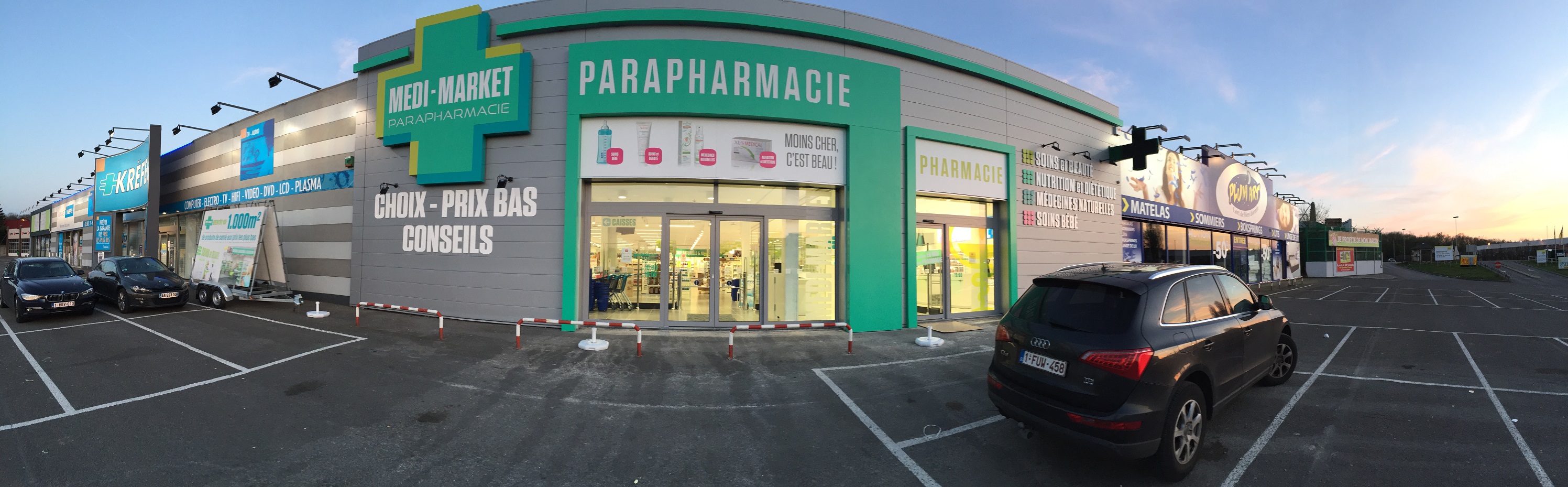 Façade d'une parapharmacie Medi-Market avec enseignes vertes et bleues, voitures garées devant et ciel dégagé en arrière-plan.