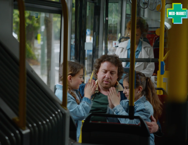 Un homme assis dans un bus avec deux jeunes filles en vestes en jean, une femme en manteau blanc à l'arrière-plan.